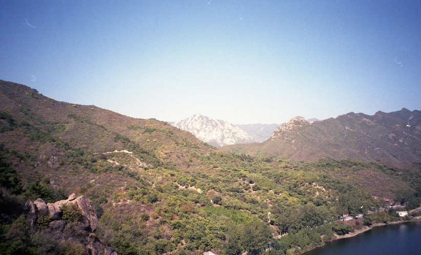 a large body of water sitting on top of a lush green hillside, inspired by Li Keran, disposable camera photograph, great wall, snow capped mountains, coloured film photography