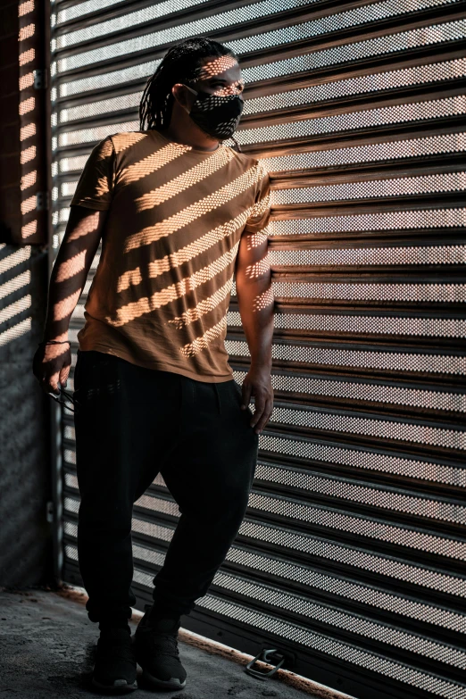 a man standing in front of a metal door, pexels contest winner, black fine lines on warm brown, wearing stripe shirt, with backlight, wearing pants and a t-shirt