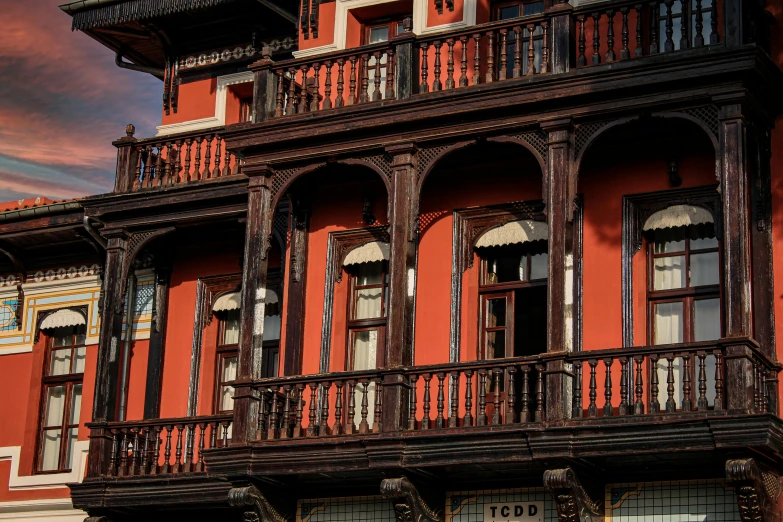 a red building with a clock on the front of it, inspired by Luis Paret y Alcazar, pexels contest winner, art nouveau, elaborate carved wood balconies, shot with sony alpha 1 camera, square, red and orange colored