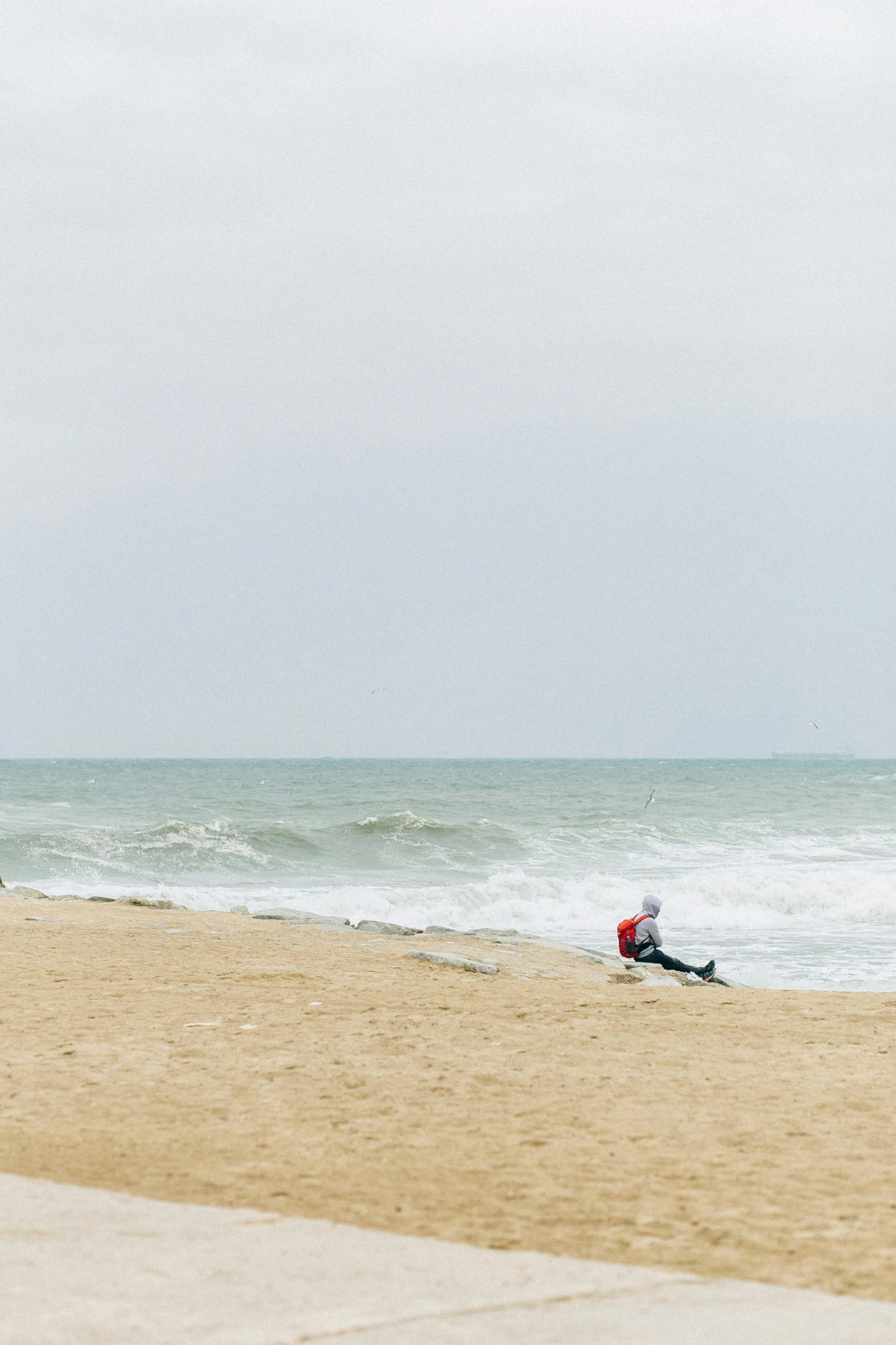 a man sitting on top of a sandy beach next to the ocean, by Daniel Seghers, minimalism, surf photography, stormy day, normandy, sittin