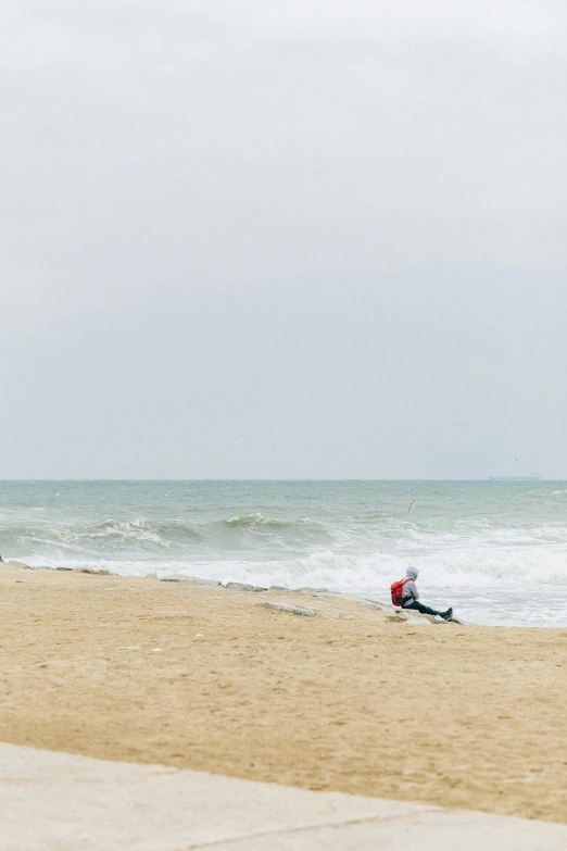 a man sitting on top of a sandy beach next to the ocean, by Daniel Seghers, minimalism, surf photography, stormy day, normandy, sittin