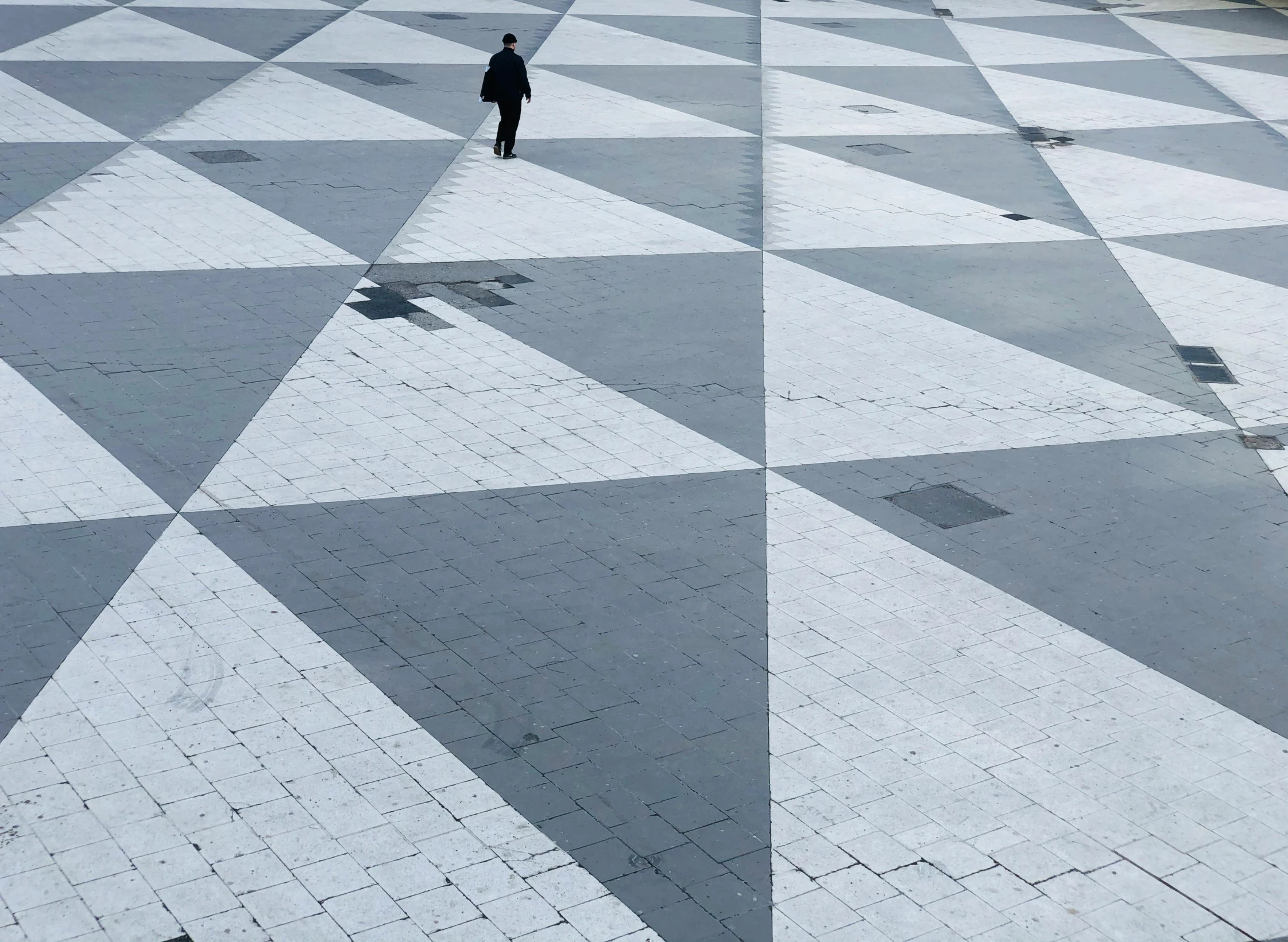 a person walking across a black and white checkered floor, an album cover, pexels contest winner, precisionism, landscape of geometric shapes, santiago calatrava, monocolor mosaics, plaza