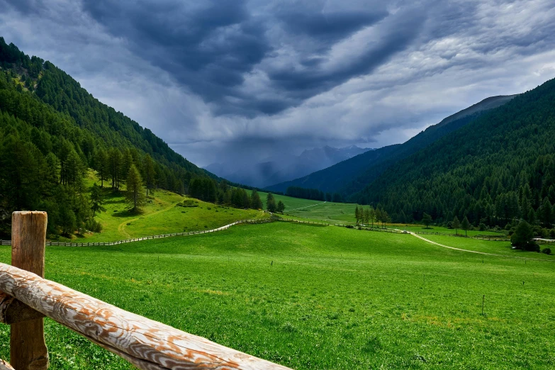 a wooden fence sitting in the middle of a lush green field, by Matthias Stom, pexels contest winner, in an epic valley, stormclouds, conde nast traveler photo, pastures