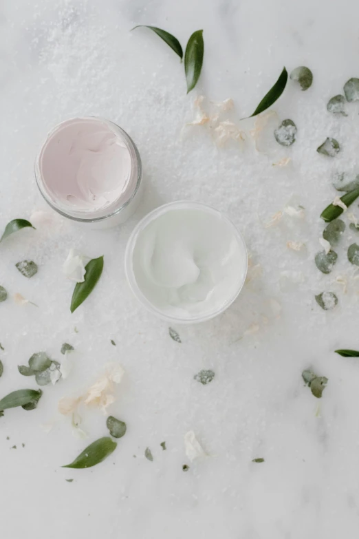 two jars of cream sitting on top of a white table, by Lucette Barker, trending on pexels, renaissance, eucalyptus, white facepaint, white and pink, while marble