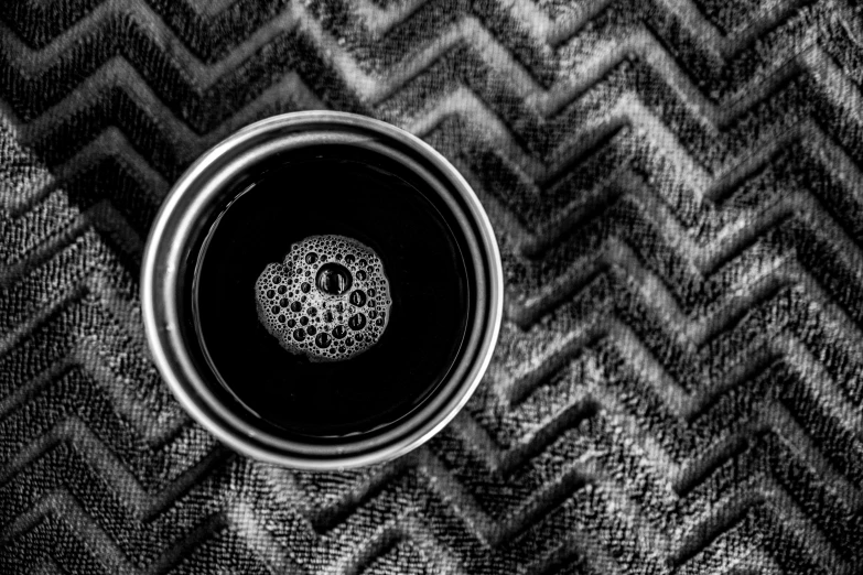 a cup of coffee sitting on top of a table, a stipple, by Daniel Gelon, pexels contest winner, op art, black and white zig zag floor, cloth and metal, made of ferrofluid, # macro