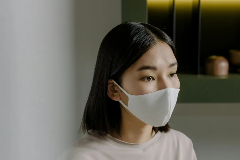a woman wearing a face mask in a kitchen, inspired by Kanō Naizen, trending on pexels, sōsaku hanga, on grey background, silicone skin, wearing white silk, angle view