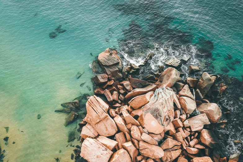 a group of rocks sitting on top of a body of water, by Lee Loughridge, unsplash contest winner, helicopter view, brown and cyan color scheme, australian beach, slightly pixelated