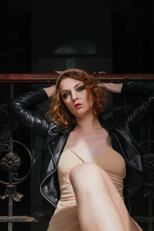 a woman in a tan dress and a black leather jacket, an album cover, inspired by Nan Goldin, unsplash, renaissance, hr ginger, stoya, casual pose, curls and curves