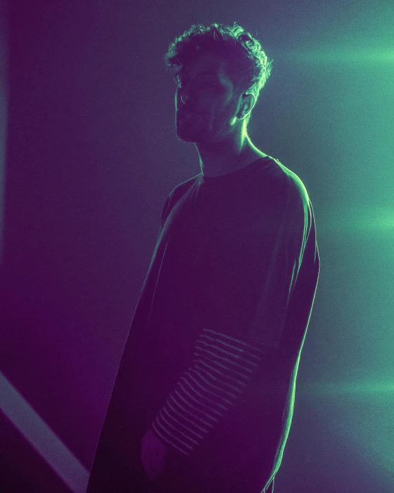 a man standing in front of a neon light, inspired by Elsa Bleda, unsplash, wearing a green sweater, zayn malik, desaturated, profile pose