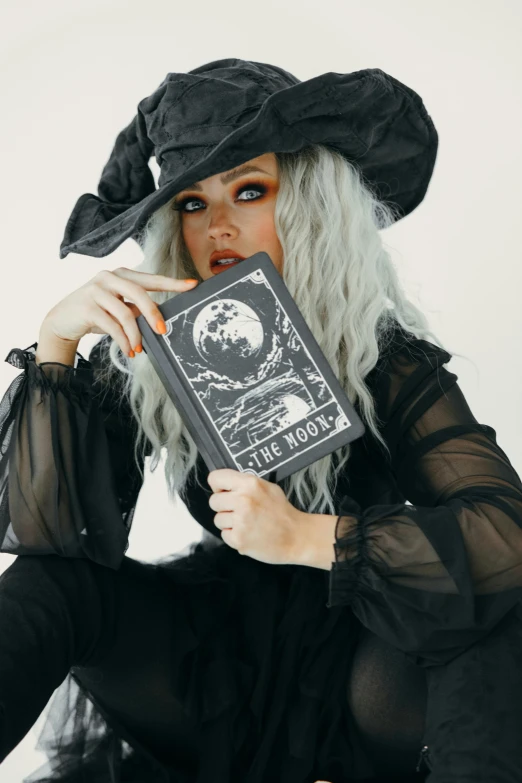 a woman in a witch costume holding a book, an album cover, by Robbie Trevino, lunar themed attire, grey, holding notebook, lookbook