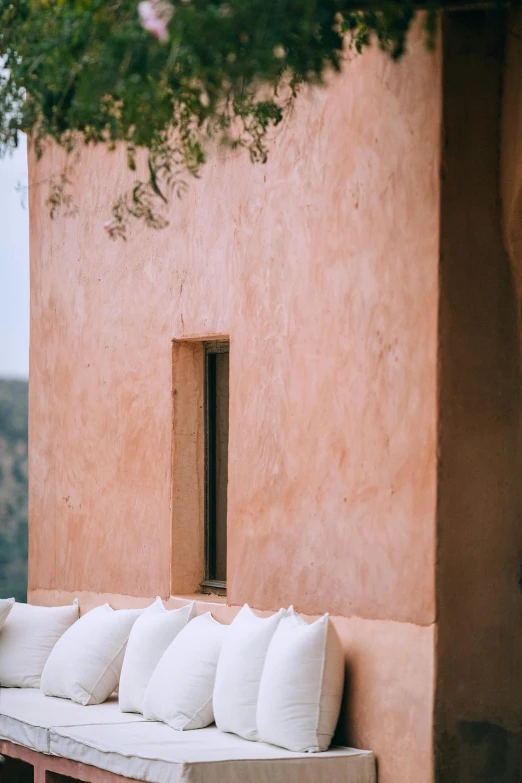 a group of white pillows sitting on top of a wooden bench, a picture, inspired by Ricardo Bofill, trending on unsplash, les nabis, pink color scheme, mediterranean architecture, ocher, looking from side