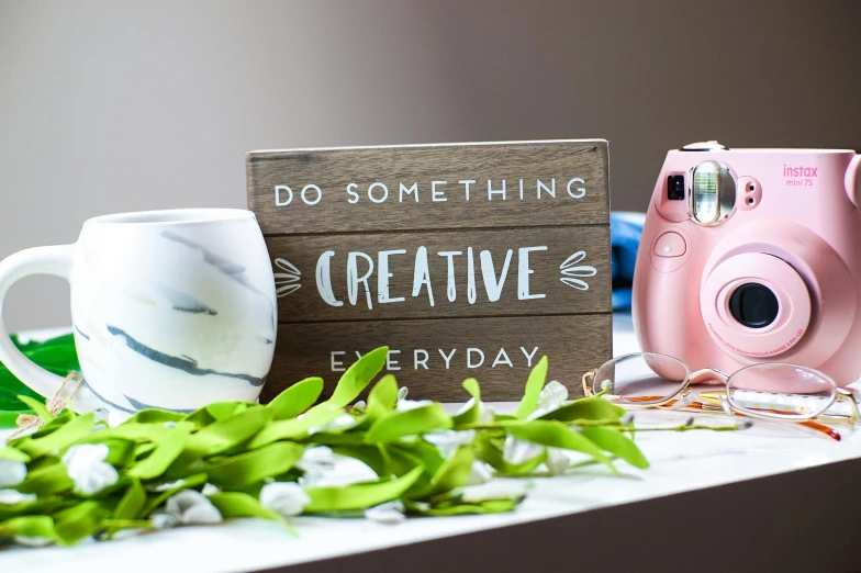 a camera sitting on top of a table next to a cup, inspired by Eden Box, graffiti, crafts and more, my little everything, sign, product photograph