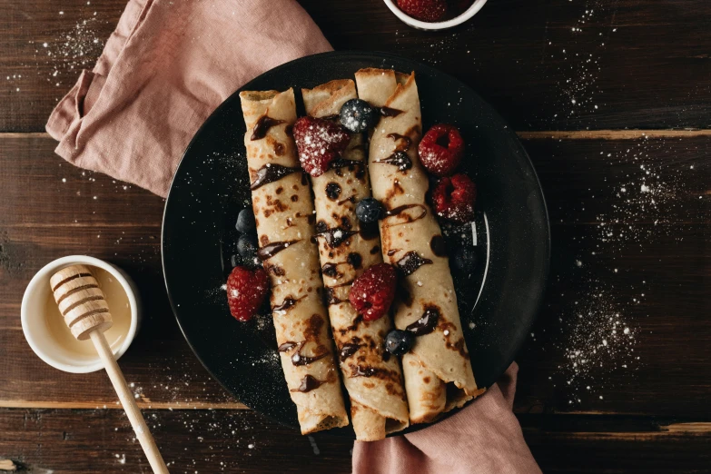 a black plate topped with crepes and berries, unsplash, very long arms, detailed product image, brown, background image