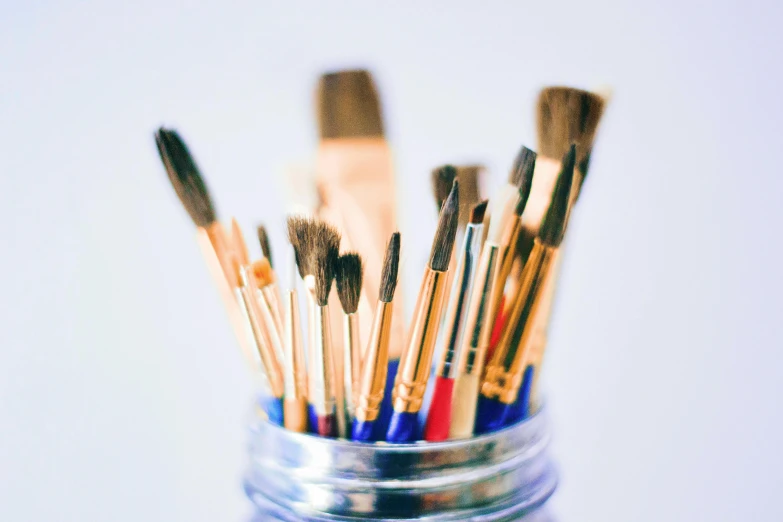 a jar filled with paint brushes sitting on top of a table, pexels, visual art, plain background, instagram post, brightly lit, no - text no - logo