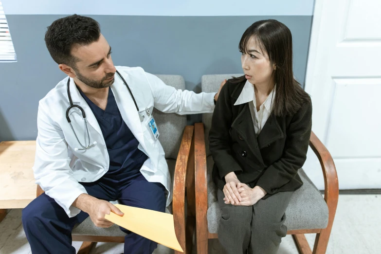 a doctor talking to a woman sitting in a chair, a colorized photo, pexels contest winner, asian male, cysts, praised, brown