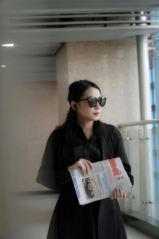 a woman standing on a balcony holding a newspaper, inspired by Cheng Jiasui, reddit, private press, wearing shiny black goggles, jakarta, airport, high quality photo