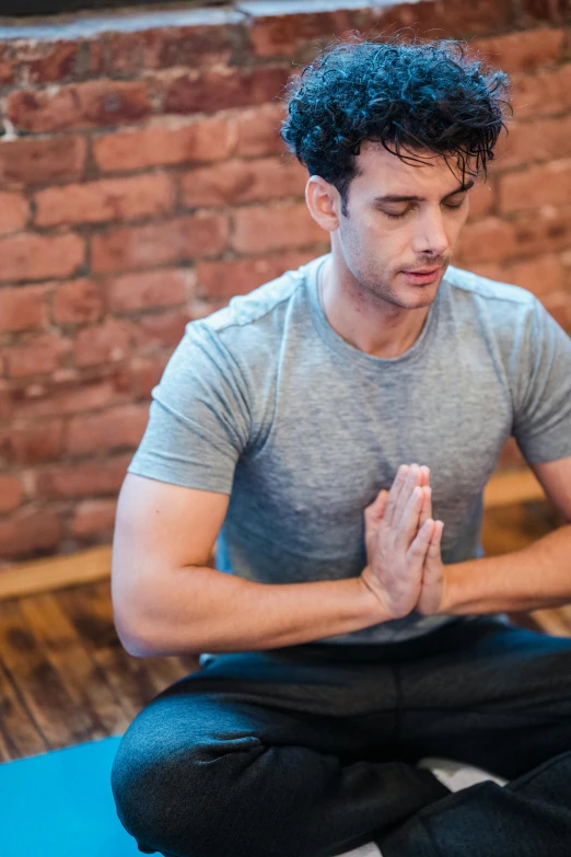 a man sitting on a yoga mat in front of a brick wall, prayer hands, profile image, magnesium, steroid use