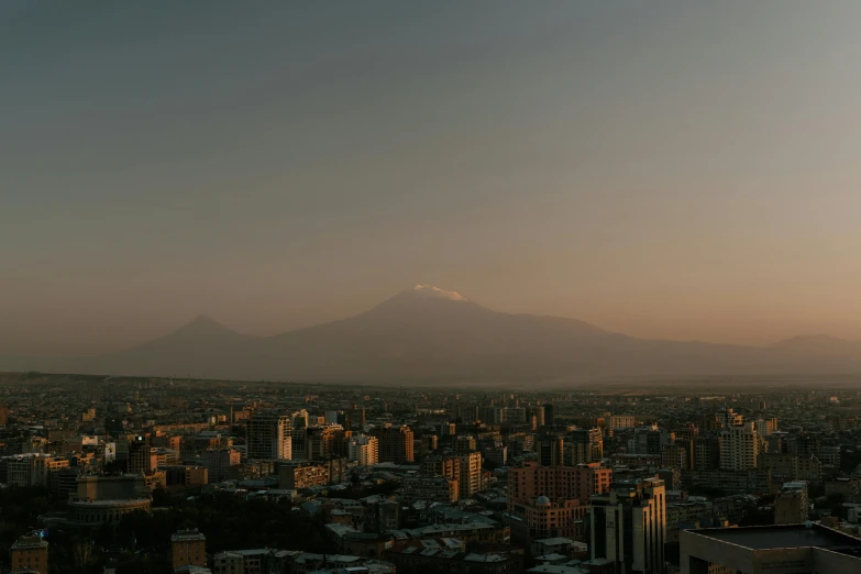 a view of a city with a mountain in the distance, pexels contest winner, hurufiyya, afternoon lighting, background image, black volcano afar, drone footage