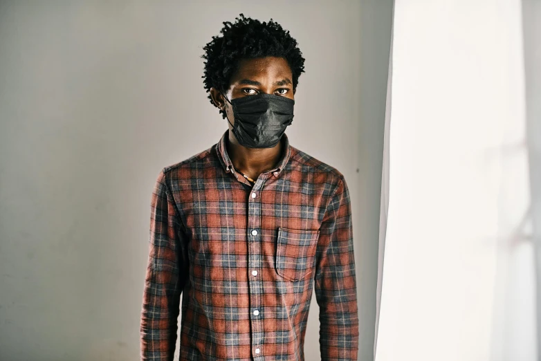 a man wearing a mask standing in front of a window, black arts movement, wearing a flannel shirt, with textured hair and skin, respirator, plain background
