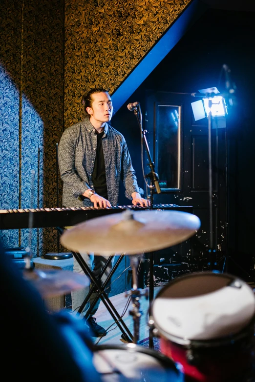 a man that is sitting in front of a keyboard, an album cover, unsplash, happening, playing drums, studio lights, 3 / 4 wide shot, standing on top of a piano