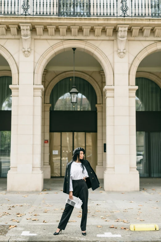 a woman walking down a sidewalk in front of a building, trending on unsplash, paris school, long curvy black hair, archway, white and black clothing, wearing jacket and skirt