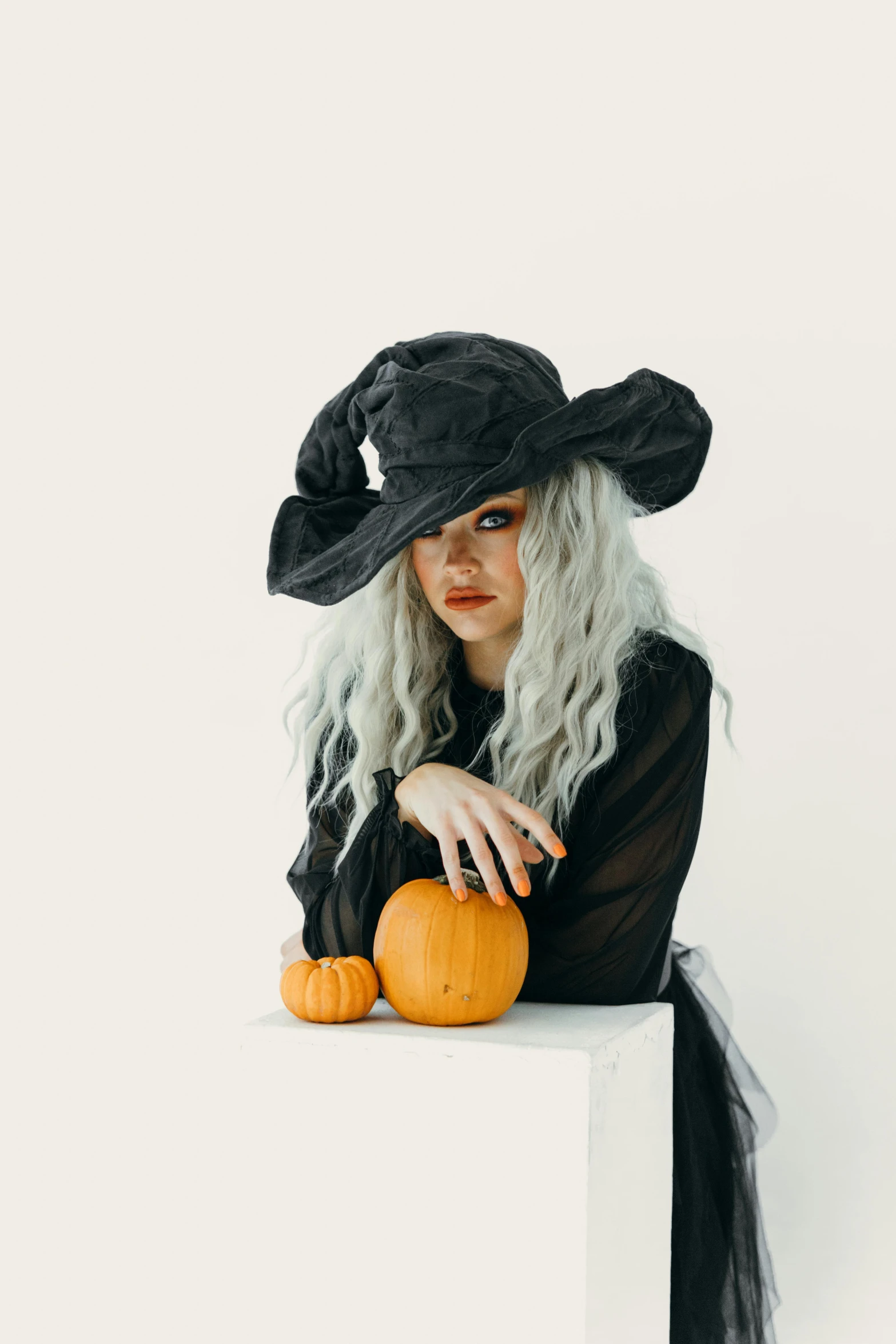 a woman wearing a witch hat and holding a pumpkin, pexels, gothic art, curled silver hair, on a white table, gif