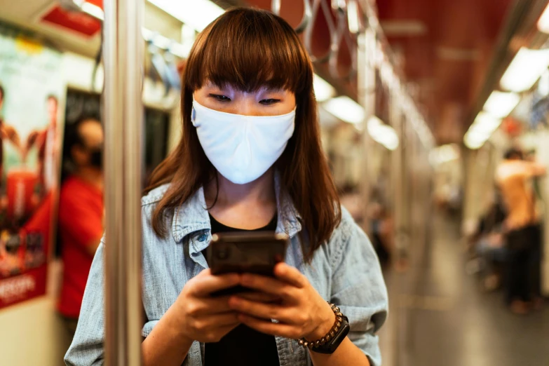 a woman wearing a face mask while looking at her phone, happening, square, mrt, scientific, getty images