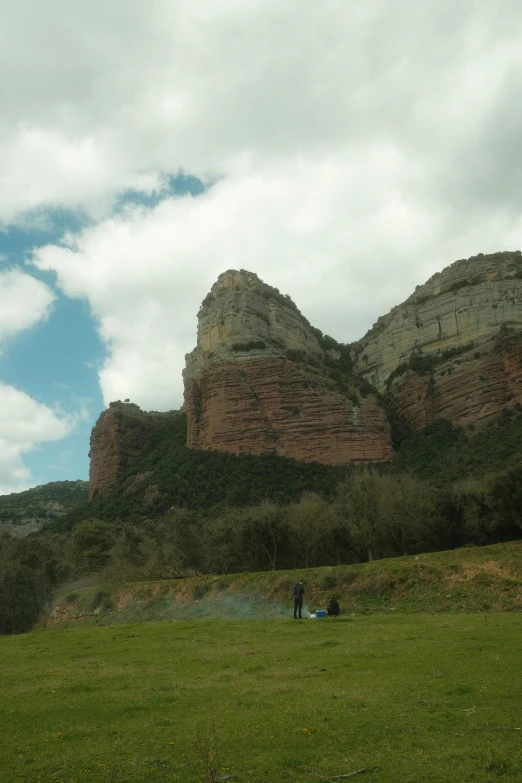 a man flying a kite on top of a lush green field, by Gaudi, les nabis, large rocky mountain, menacing!!!, two hovering twin nuns, monserrat gudiol