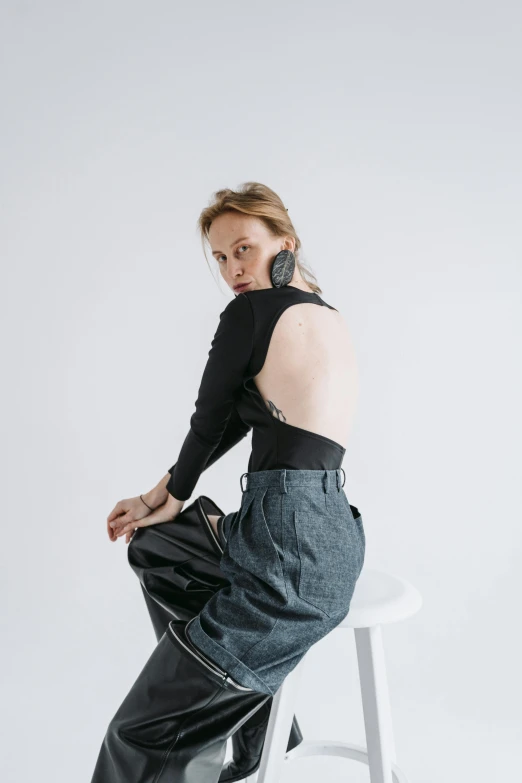 a woman sitting on top of a white stool, an album cover, by Nina Hamnett, trending on pexels, renaissance, baggy jeans, model エリサヘス s from acquamodels, showing her shoulder from back, black turtleneck