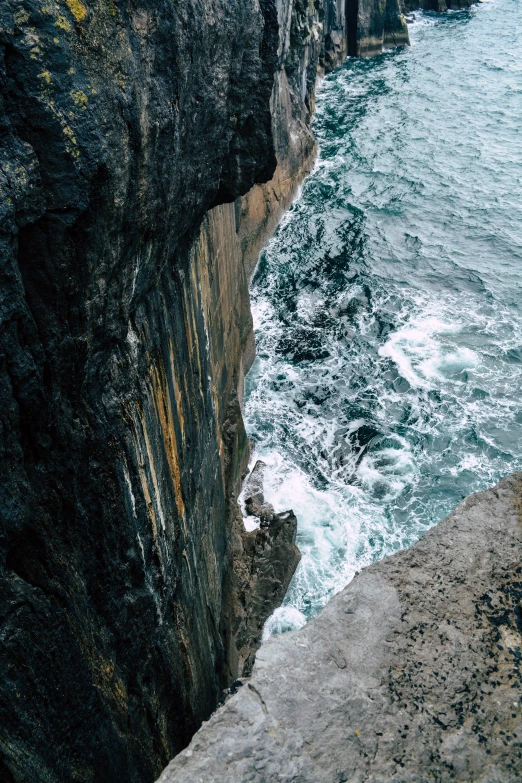 a man standing on top of a cliff next to the ocean, pexels contest winner, detail texture, deep chasm, orkney islands, falling off a cliff