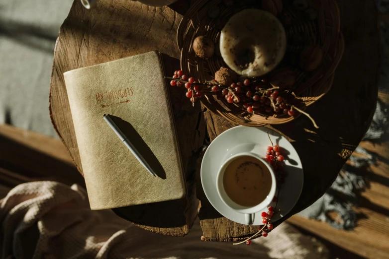 a wooden table topped with a cup of coffee and a book, luxury journal cover, found scribbled in a notebook, thumbnail, cottagecore