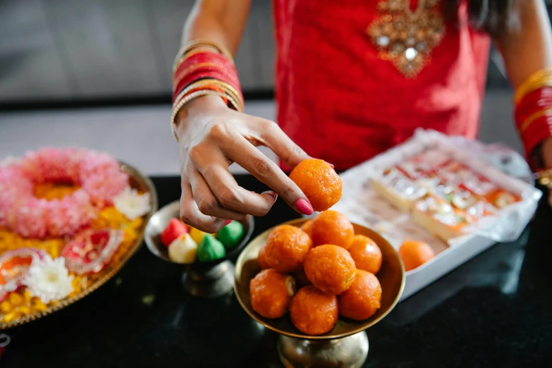 a close up of a person putting food in a bowl, by Julia Pishtar, hindu ornaments, a table full of candy, square, thumbnail