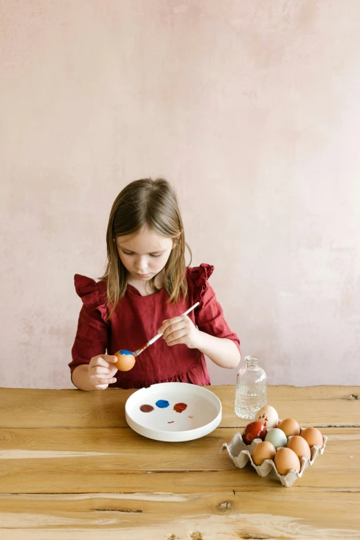 a little girl painting eggs on a wooden table, inspired by Frieke Janssens, pexels contest winner, prussian blue and venetian red, helene frankenthaler, promotional image, plating