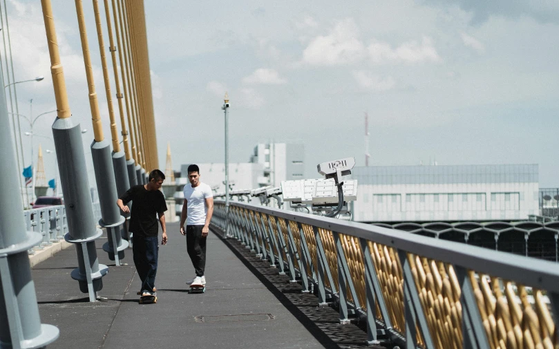 a couple of men riding skateboards across a bridge, a picture, by Niko Henrichon, unsplash, happening, akikazu mizuno, outlive streetwear collection, skybridge towers, person in foreground