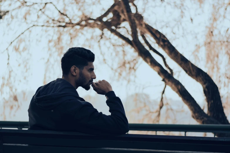 a man sitting on a bench talking on a cell phone, a picture, trending on pexels, hurufiyya, looking off to the side, profile image, melancholic, raphael lecoste