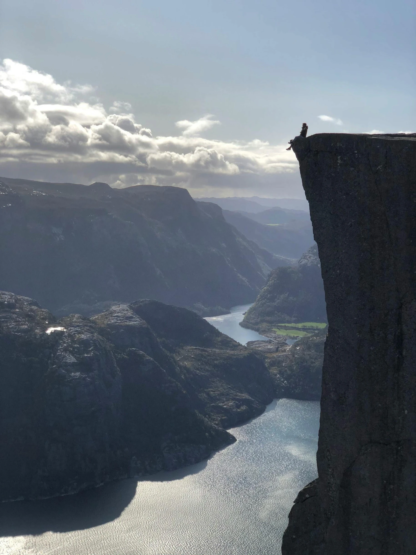 a person standing on the edge of a cliff, by Tom Wänerstrand, happening, fjord, that is 1300 feet tall, photo taken in 2018, multiple stories