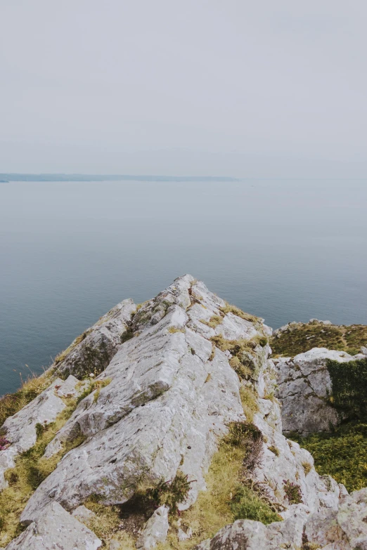 a person standing on top of a mountain next to a body of water, ireland, calm sea, calmly conversing 8k, ultrawide image