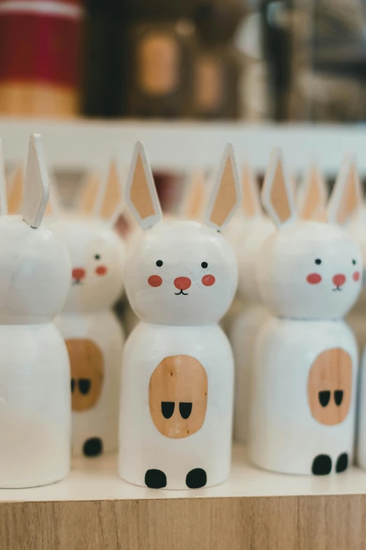 a group of wooden bunny figurines sitting on top of a table, a cartoon, inspired by Nara Yoshitomo, trending on unsplash, folk art, sitting on a store shelf, bottle, closeup of arms, large ears