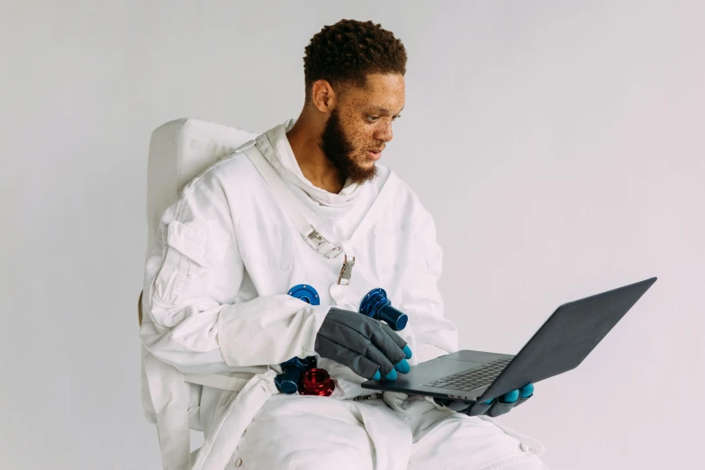 a man sitting on a chair with a laptop, inspired by Paul Georges, pexels contest winner, afrofuturism, nasa eva suit, wearing a labcoat, pete davidson, game ready