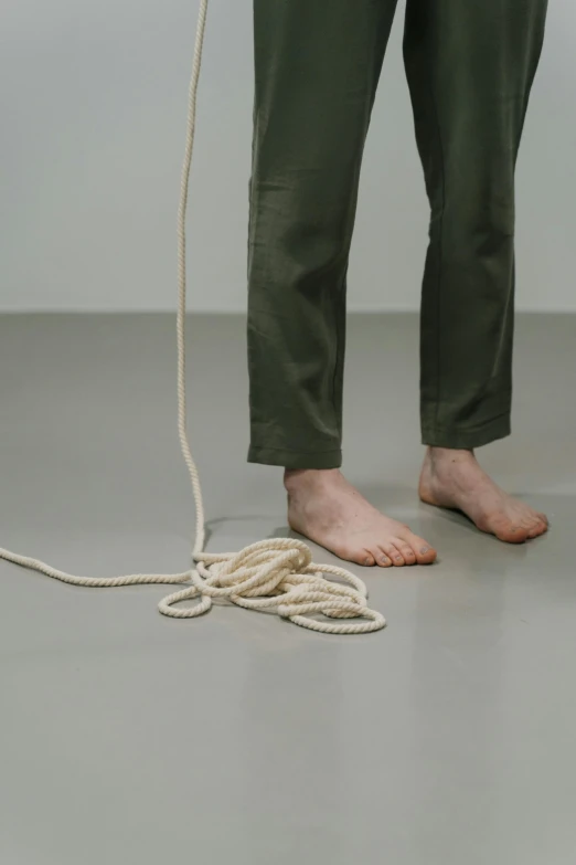 a person standing on a floor with a rope, an album cover, inspired by Bruce Nauman, pexels contest winner, realism, tangled cables, ignant, worn pants, performance