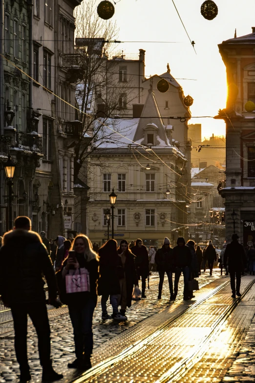 a group of people walking down a street next to tall buildings, a photo, renaissance, lviv historic centre, winter sun, lights on, crowded and populated