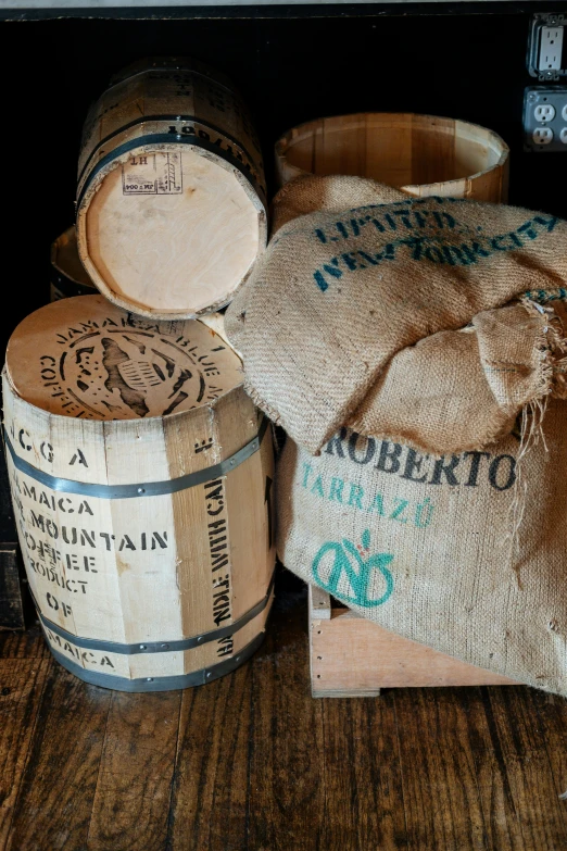 a bunch of barrels sitting on top of a wooden table, bags, arabica style, very detailed labeling, hessian cloth