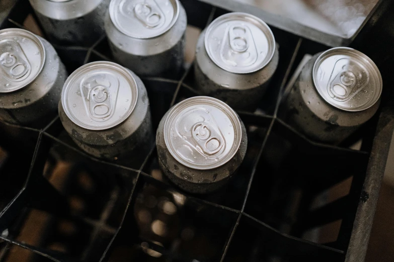 a crate filled with cans of soda sitting on top of a table, by Jakob Gauermann, pexels contest winner, grey and silver, 6 pack, slightly tanned, silver