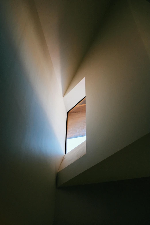 a light shines through a window in a room, an abstract sculpture, inspired by André Kertész, unsplash, light and space, narrow passage, slanted ceiling, shot from roofline, high - angle