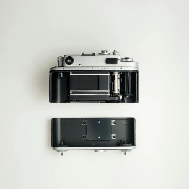 a black and silver camera sitting on top of a white wall, by Simon Gaon, unsplash, minimalism, disassembled, front and back view, isometric view from behind, retro device