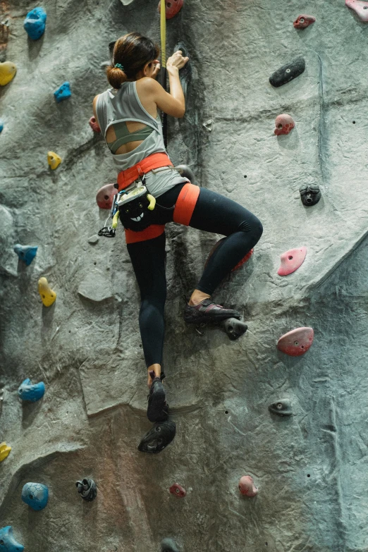 a woman climbing up the side of a rock wall, trending on pexels, indoor picture, colorized, hands on hips, scientific photo