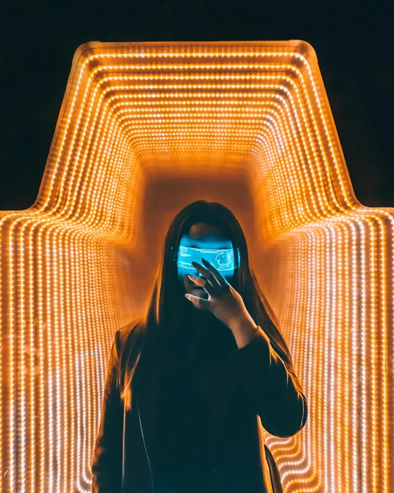 a person taking a picture with a cell phone, inspired by Beeple, pexels contest winner, holography, orange halo around her head, dimensional cyan gold led light, bisexual lighting, a person standing in front of a