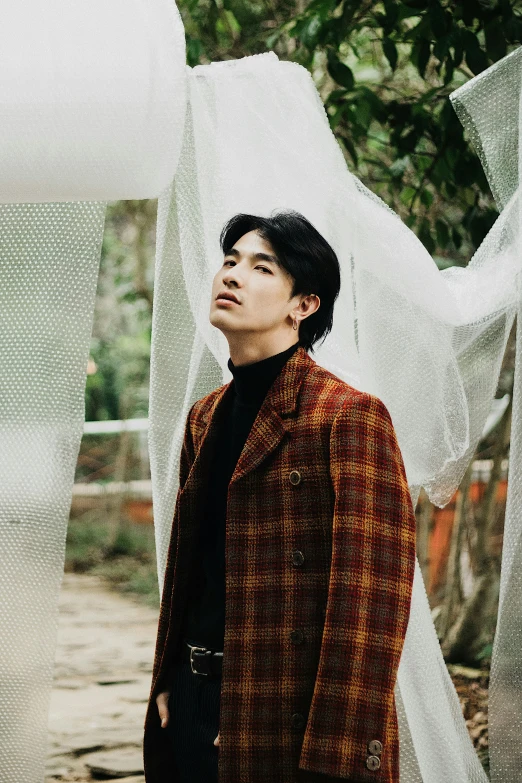 a man standing in front of a curtain, an album cover, inspired by Zhang Han, trending on pexels, brown jacket, in the garden, tartan garment, actor