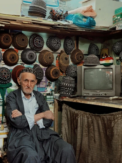 a man sitting in a chair in front of a television, by Alison Geissler, unsplash contest winner, inside an arabian market bazaar, portrait of an old, khyzyl saleem, sitting on a store shelf