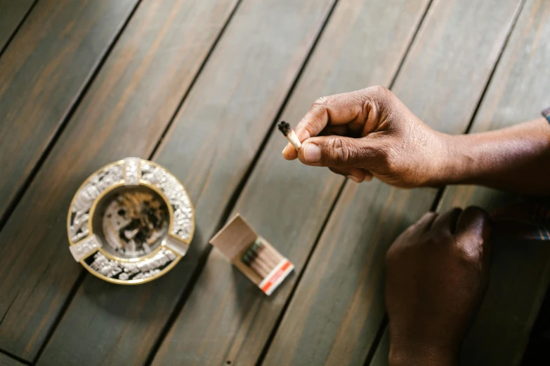 a close up of a person holding a cigarette, by Daniel Lieske, pexels contest winner, sitting on a mocha-colored table, unmistakably kenyan, botanicals, then another